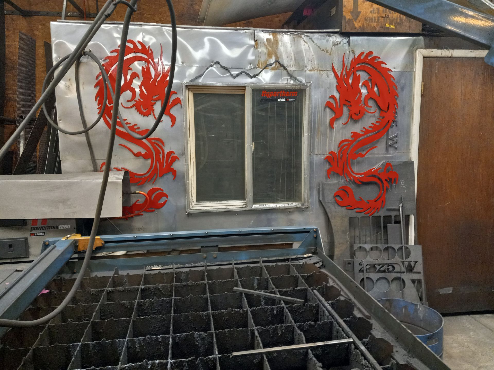 Steel panel with red dragon cutouts framing a window, above a metal cutting table.