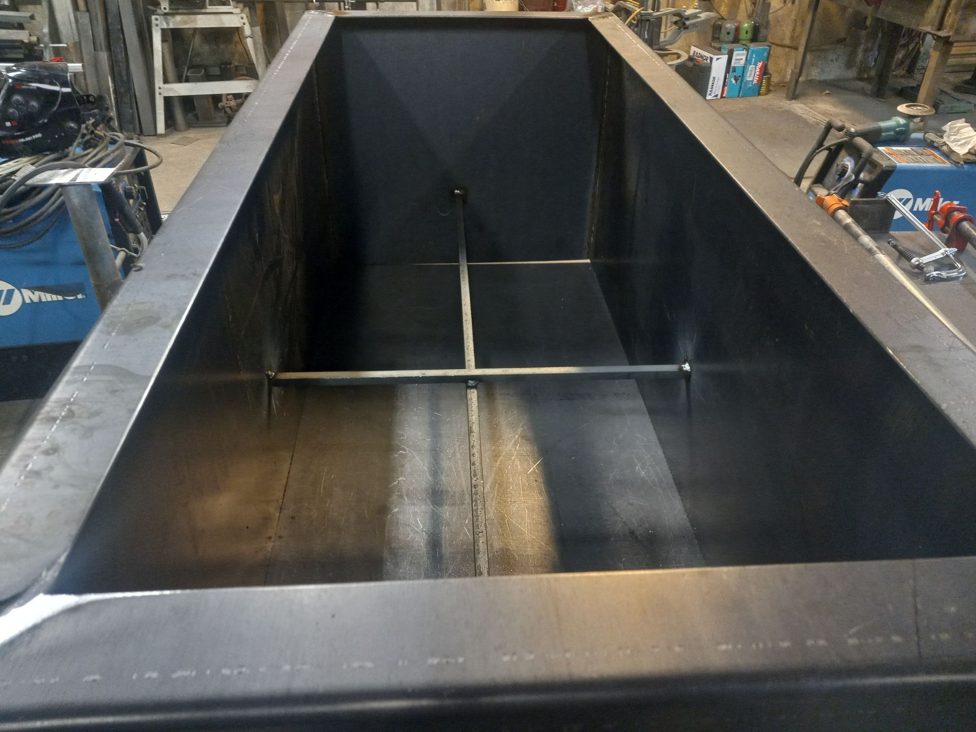 Large black metal rectangular tank with interior support beams in a workshop setting.