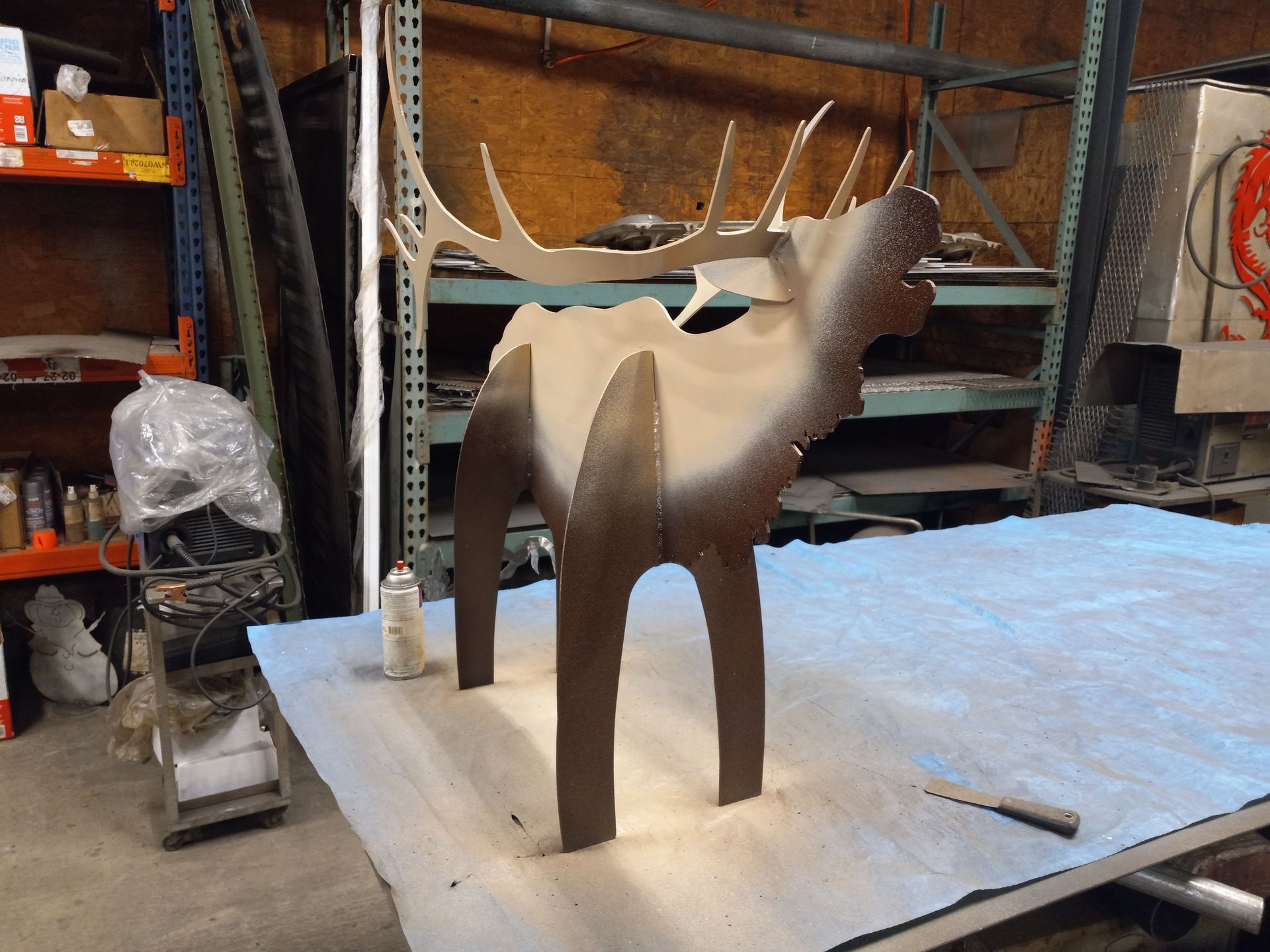 Metal elk sculpture being painted in a workshop setting. Brown and tan colors.