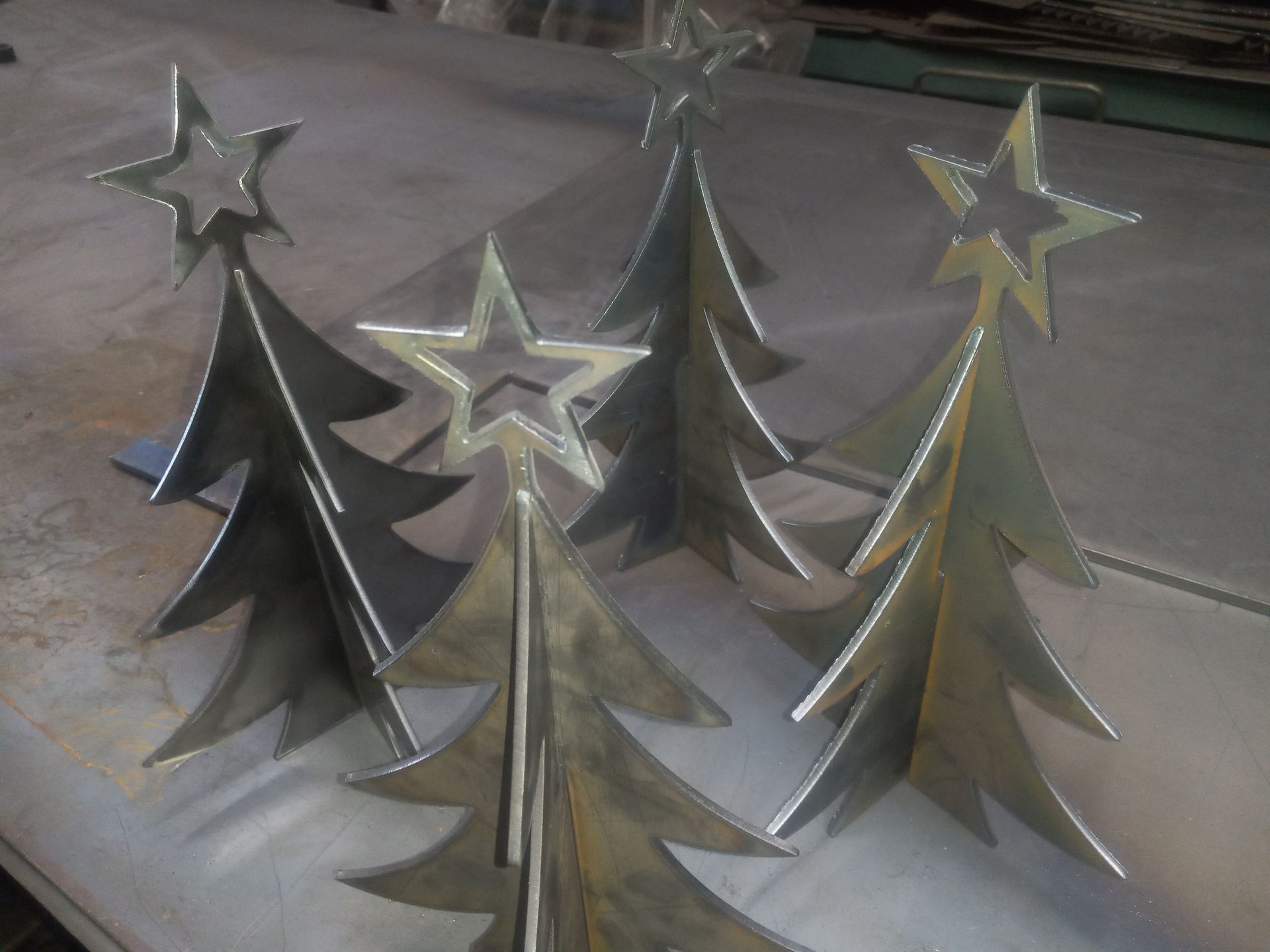 Five metal Christmas trees with star toppers sit on a metal surface.