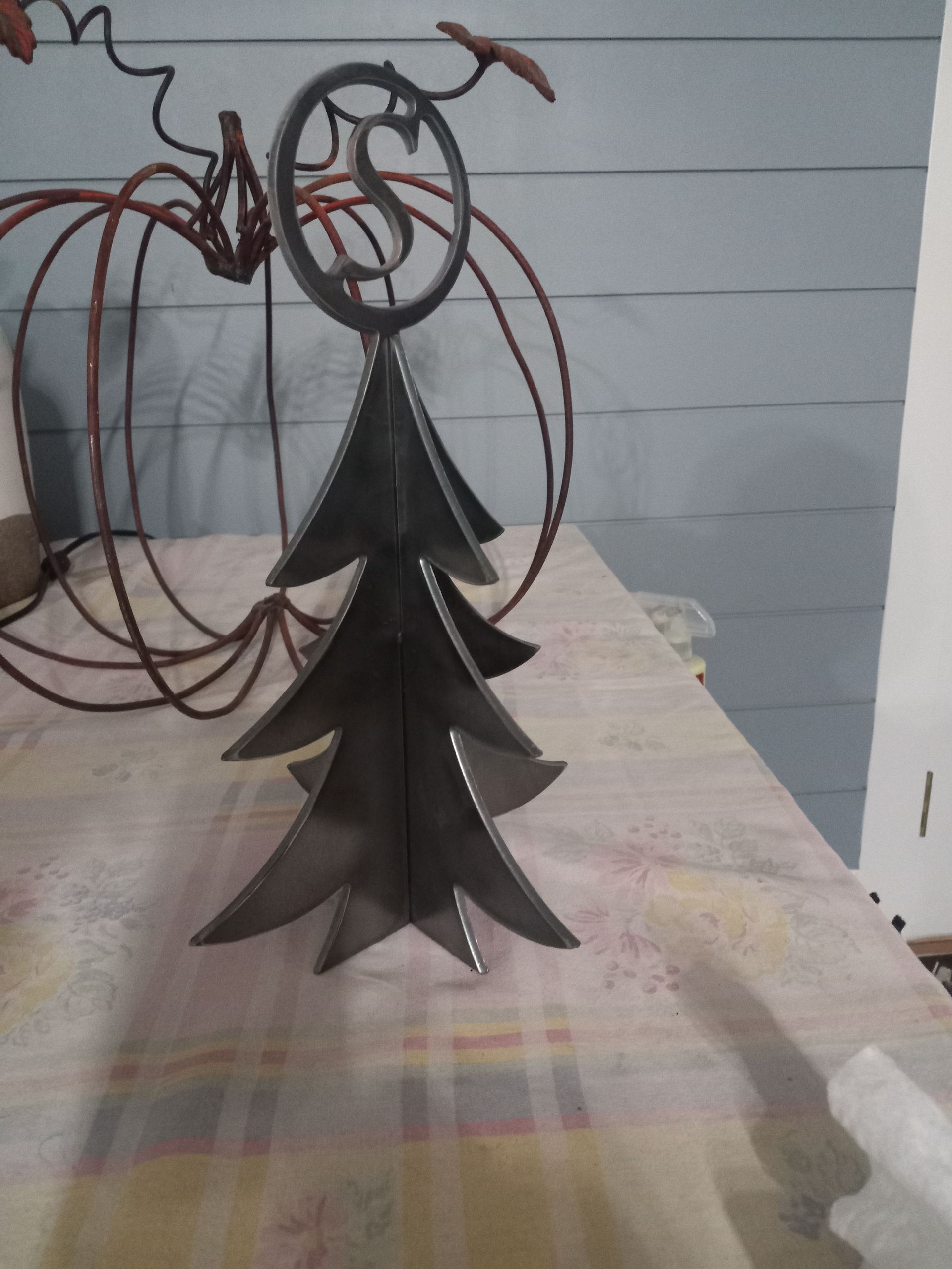 Metal Christmas tree sculpture with star, pumpkin in background.
