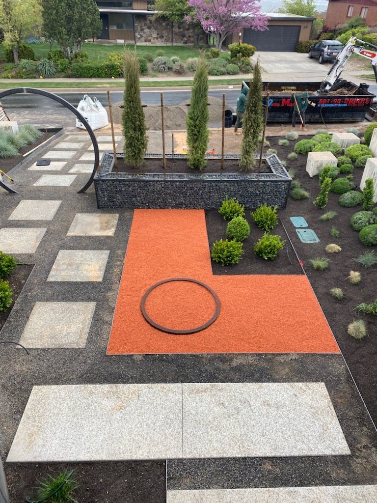 Landscaped yard with orange and gray paving stones, gravel, and Cypress trees in a planter.