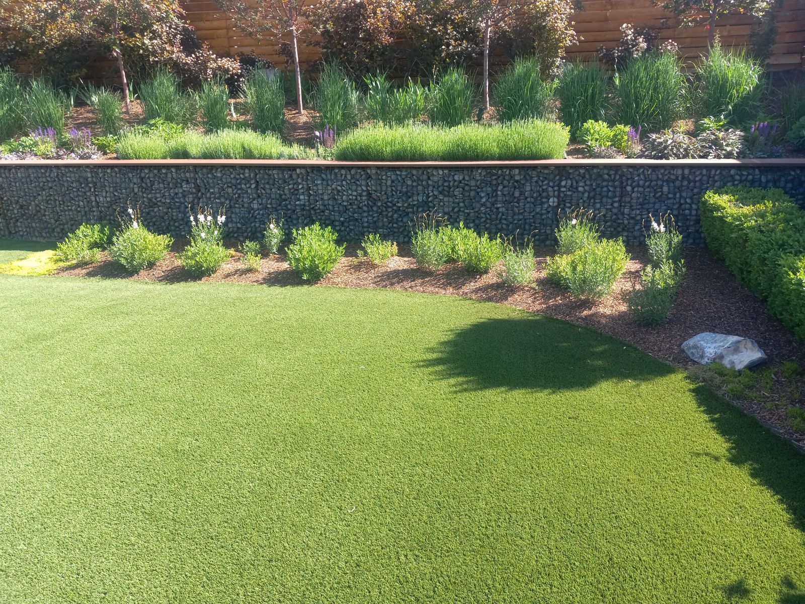 Green lawn with rock wall and lush garden.
