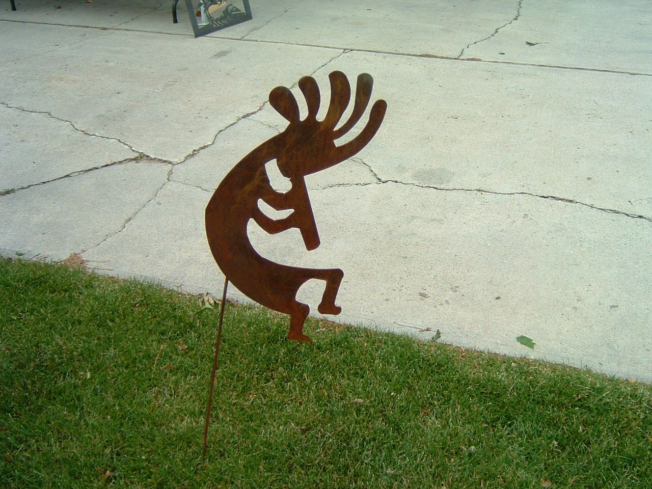 Rusty metal Kokopelli lawn decoration in green grass.