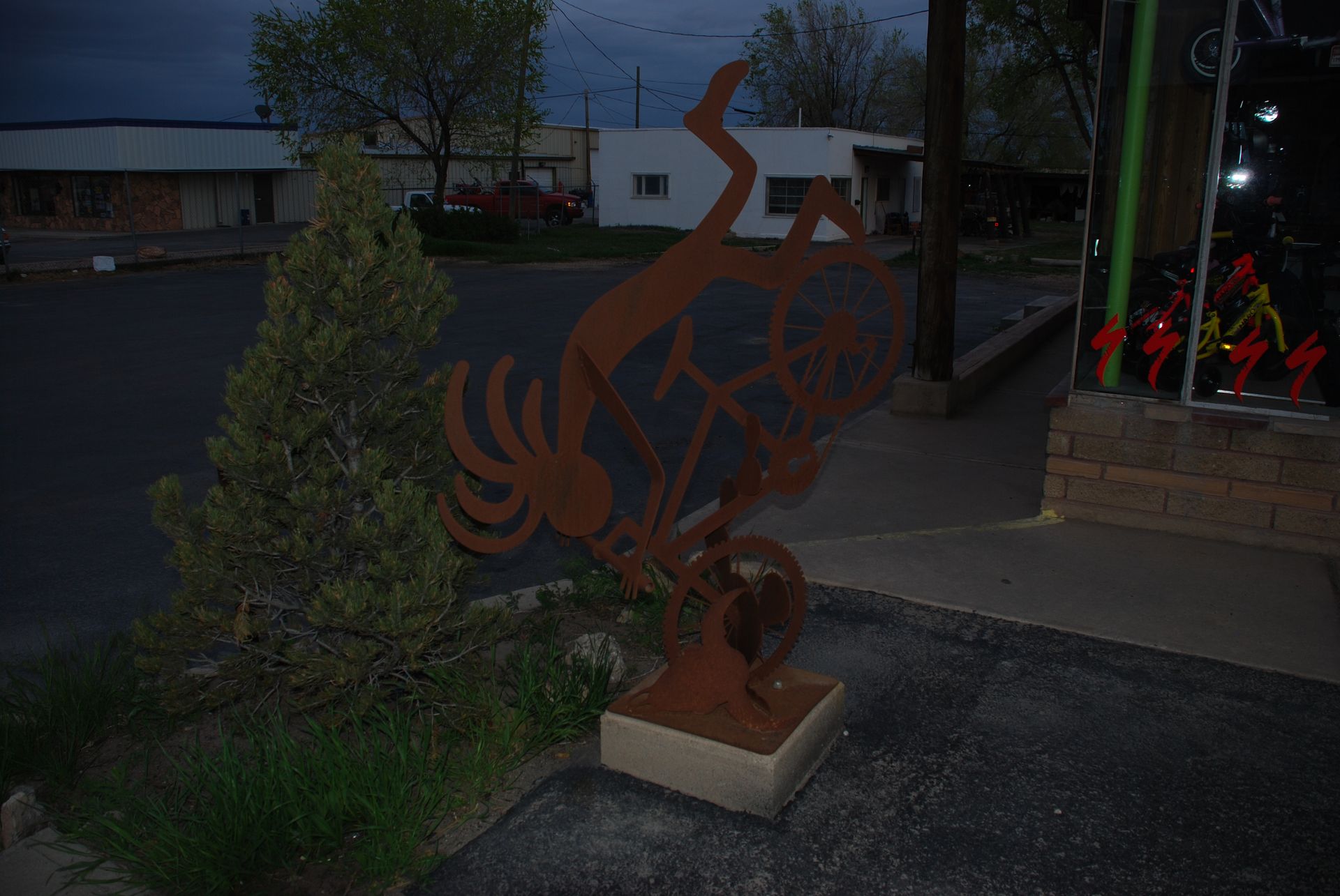 Rusty metal Kokopelli statue in front of a building at dusk.