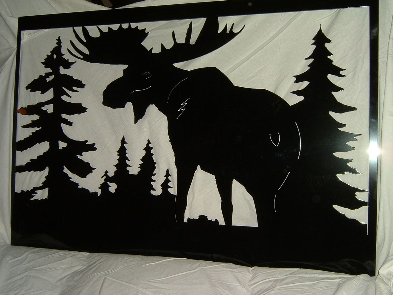 Black metal silhouette of a moose and pine trees on a white background.
