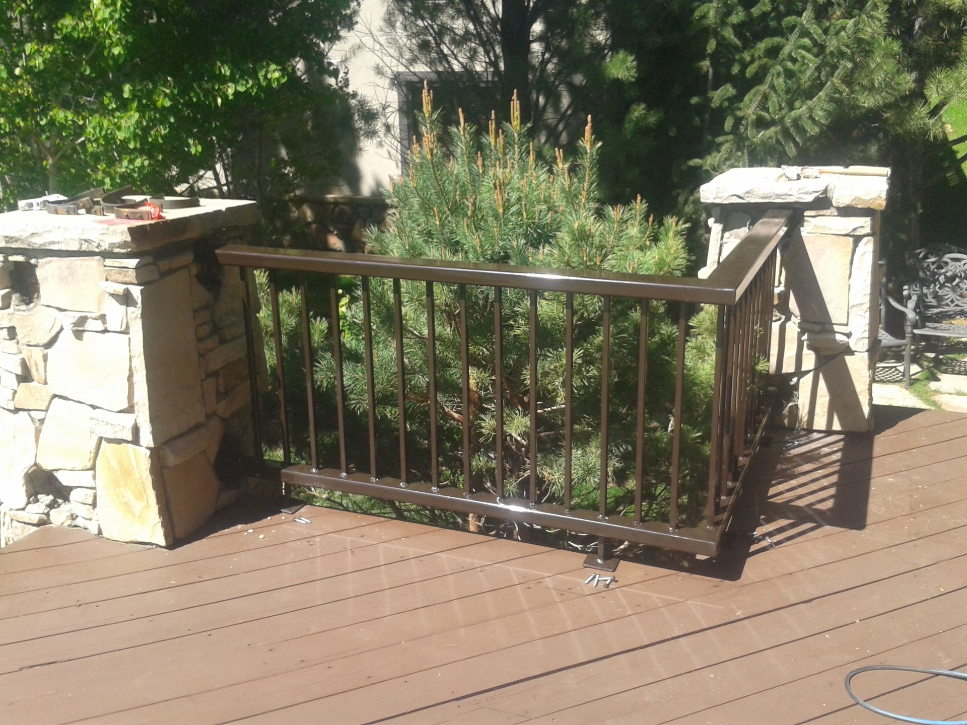 Brown metal railing on a deck between stone columns, partially obscuring a green bush.