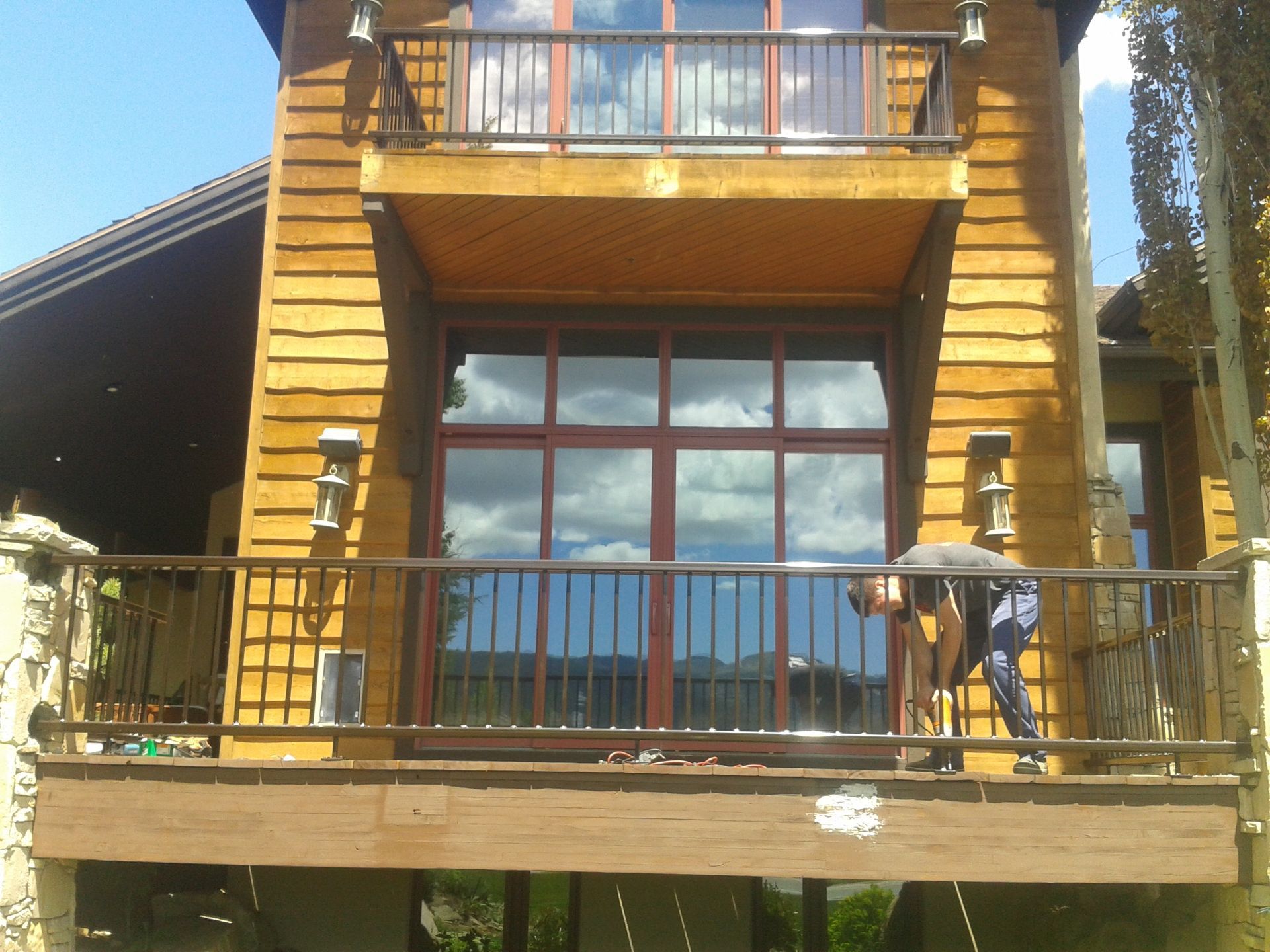 A person works on a wooden deck of a two-story building with large windows and a balcony.