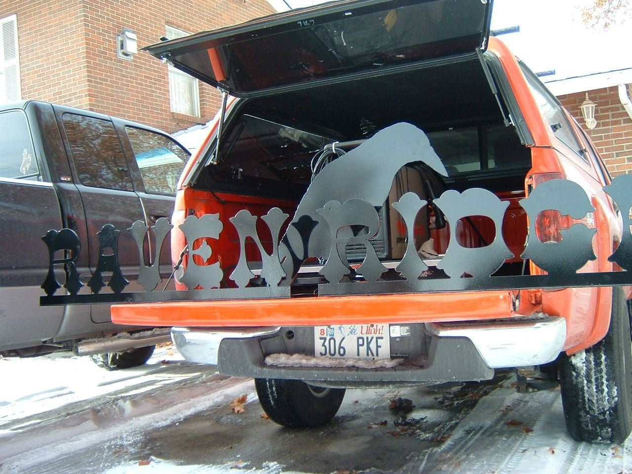 Orange pickup truck bed displaying metal cutouts, license plate visible.