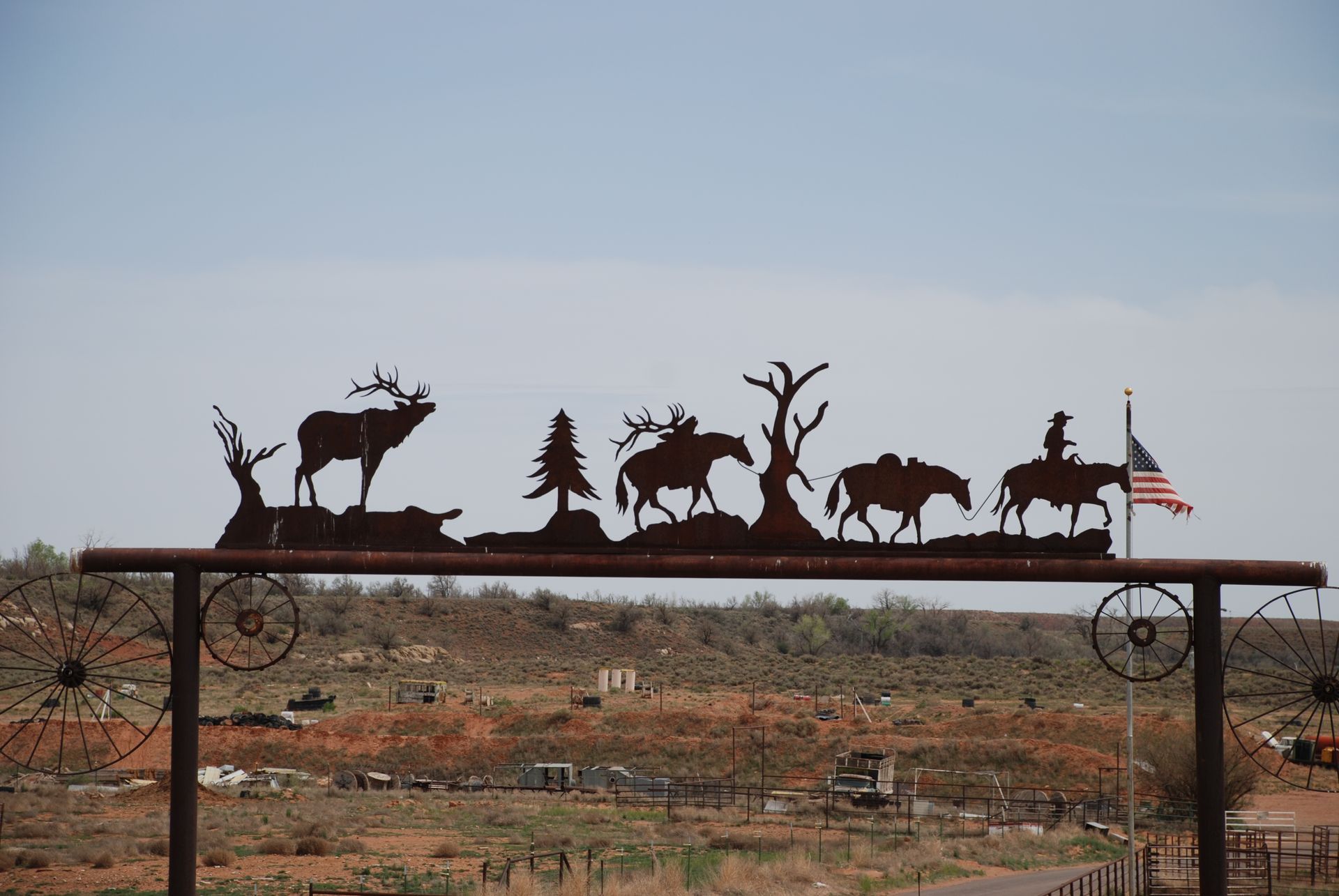 Metal archway with Western silhouettes, American flag, and landscape in background.