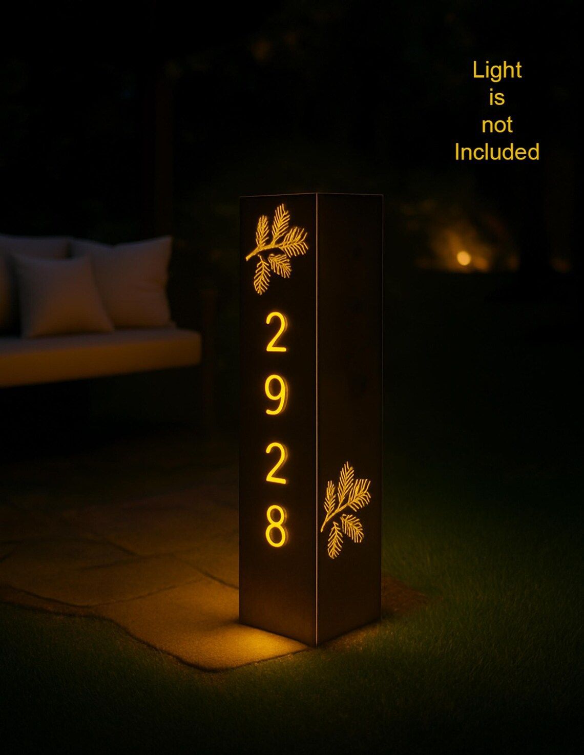 Dark brown address post illuminated with the numbers 2928. It has leaf designs and stands in a garden at night.