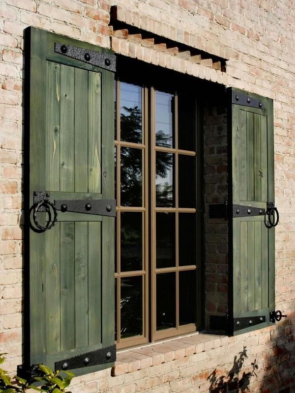 Green shutters frame a window with dark trim against a brick building.