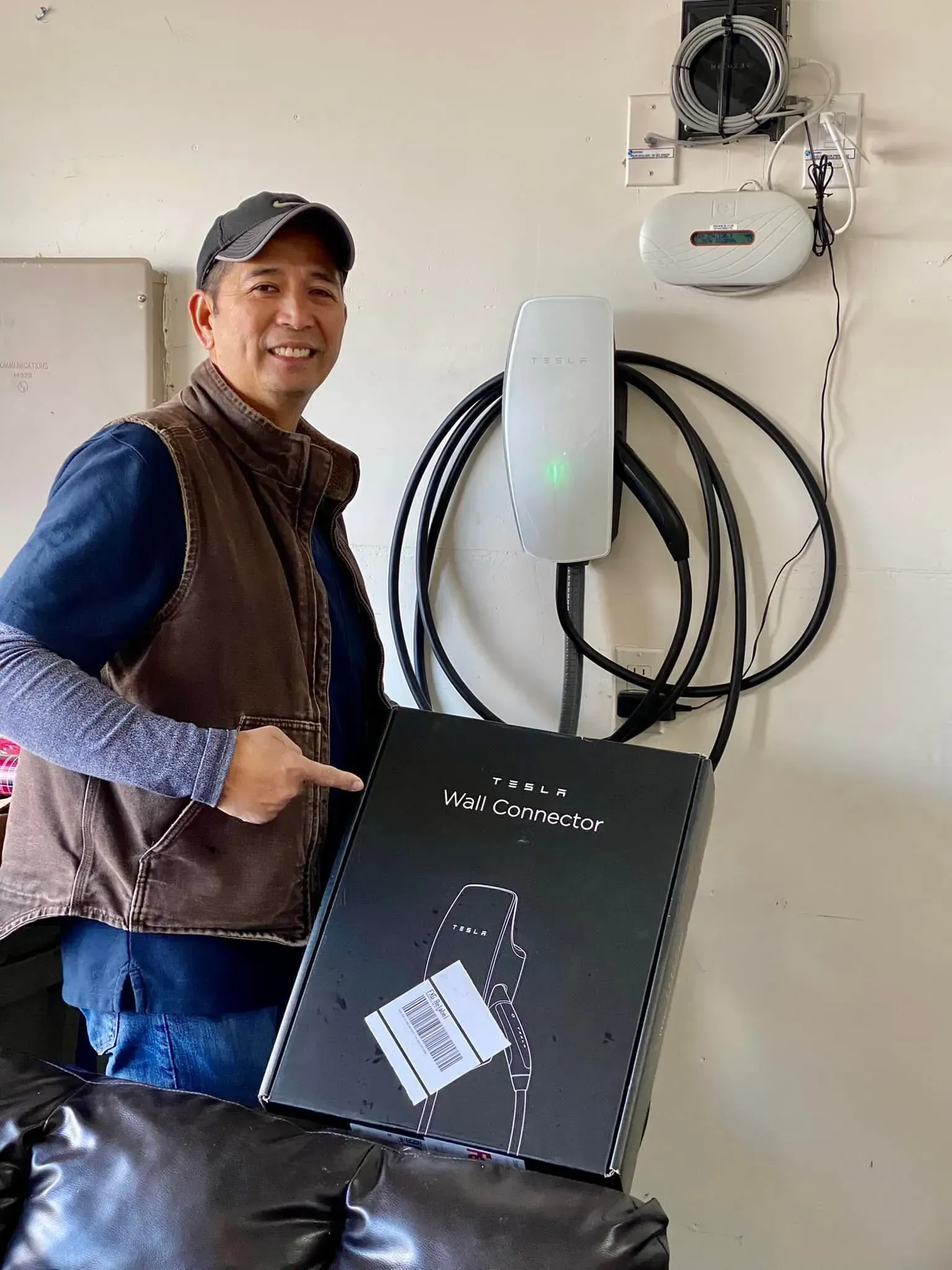 Man points to a Tesla Wall Connector box next to the installed charger on a garage wall.