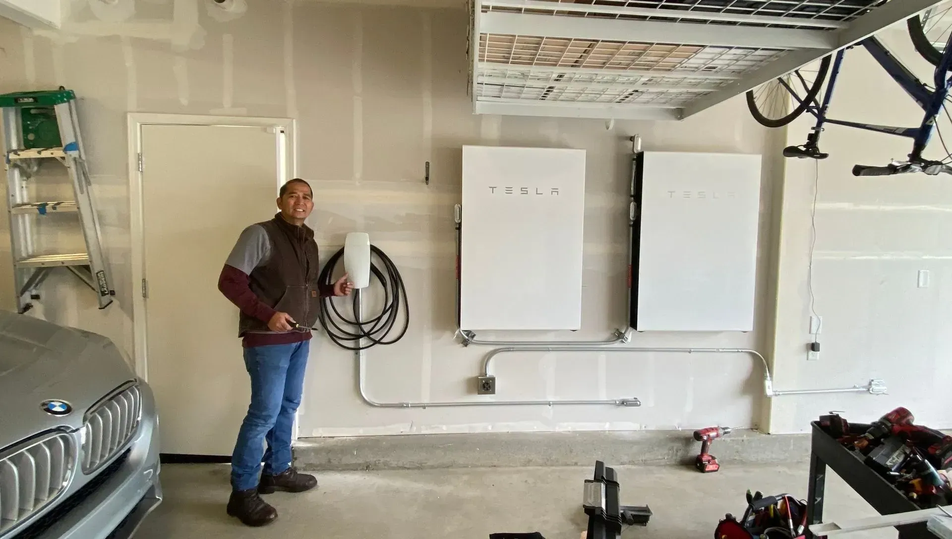 Man standing in garage with Tesla powerwalls, EV charger, and car.