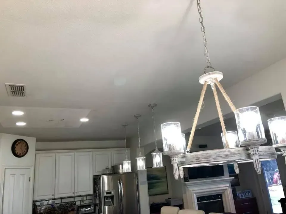 A kitchen with white cabinets, stainless steel refrigerator, and a chandelier with clear glass shades.