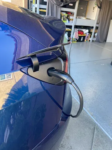 Blue Tesla charging at a home garage, charging cable plugged in.