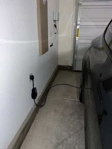 An electric vehicle charging in a garage. Black charging cable connects to a wall outlet and the car.