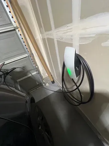 EV charger mounted on a garage wall with a charging cable connected to a car.