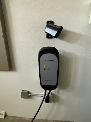 Electric vehicle charger mounted on a wall with a cable and connector, alongside a storage mount.