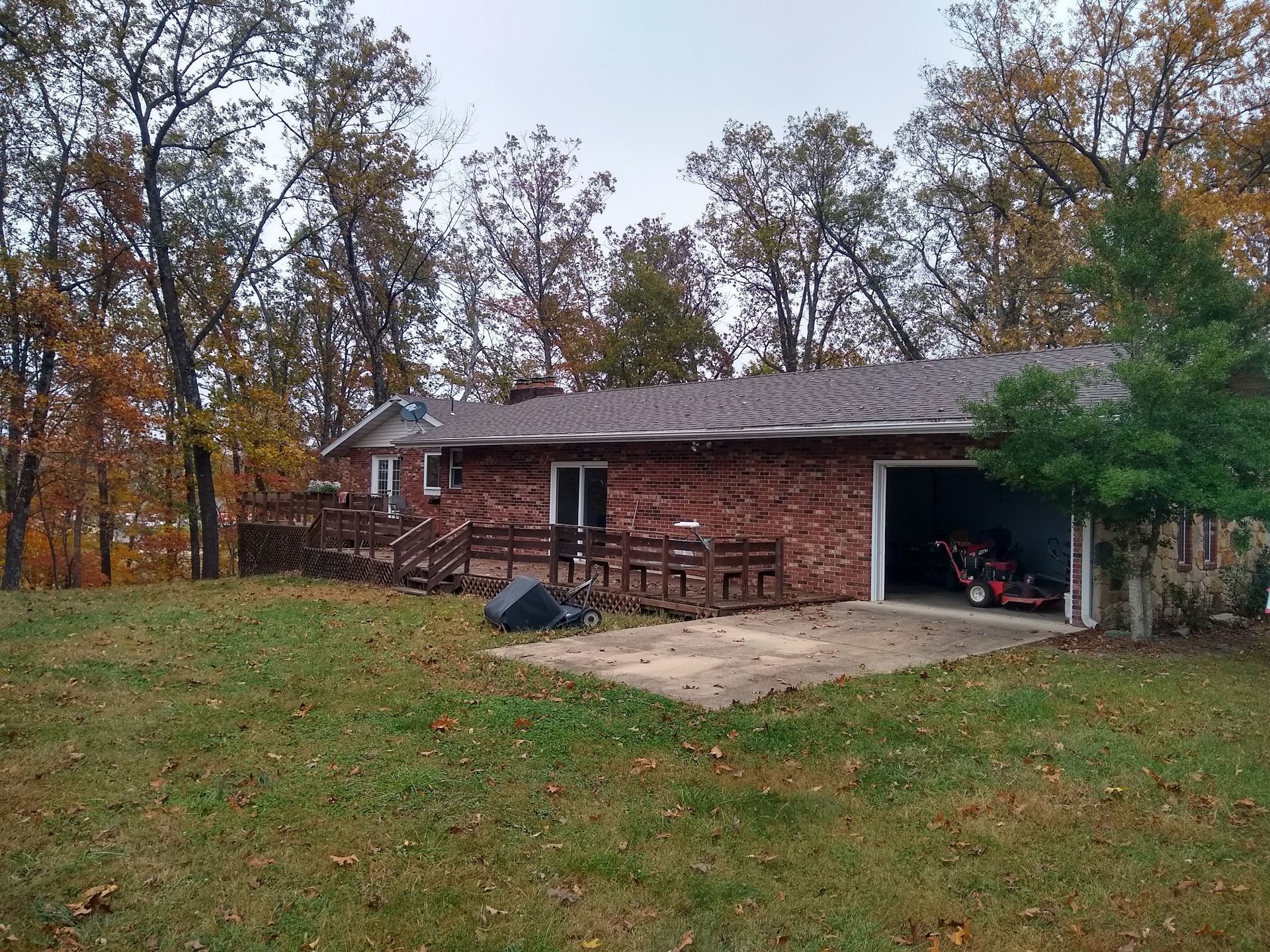 A brick house with a deck, open garage, and trees in the background. Autumn foliage on trees.