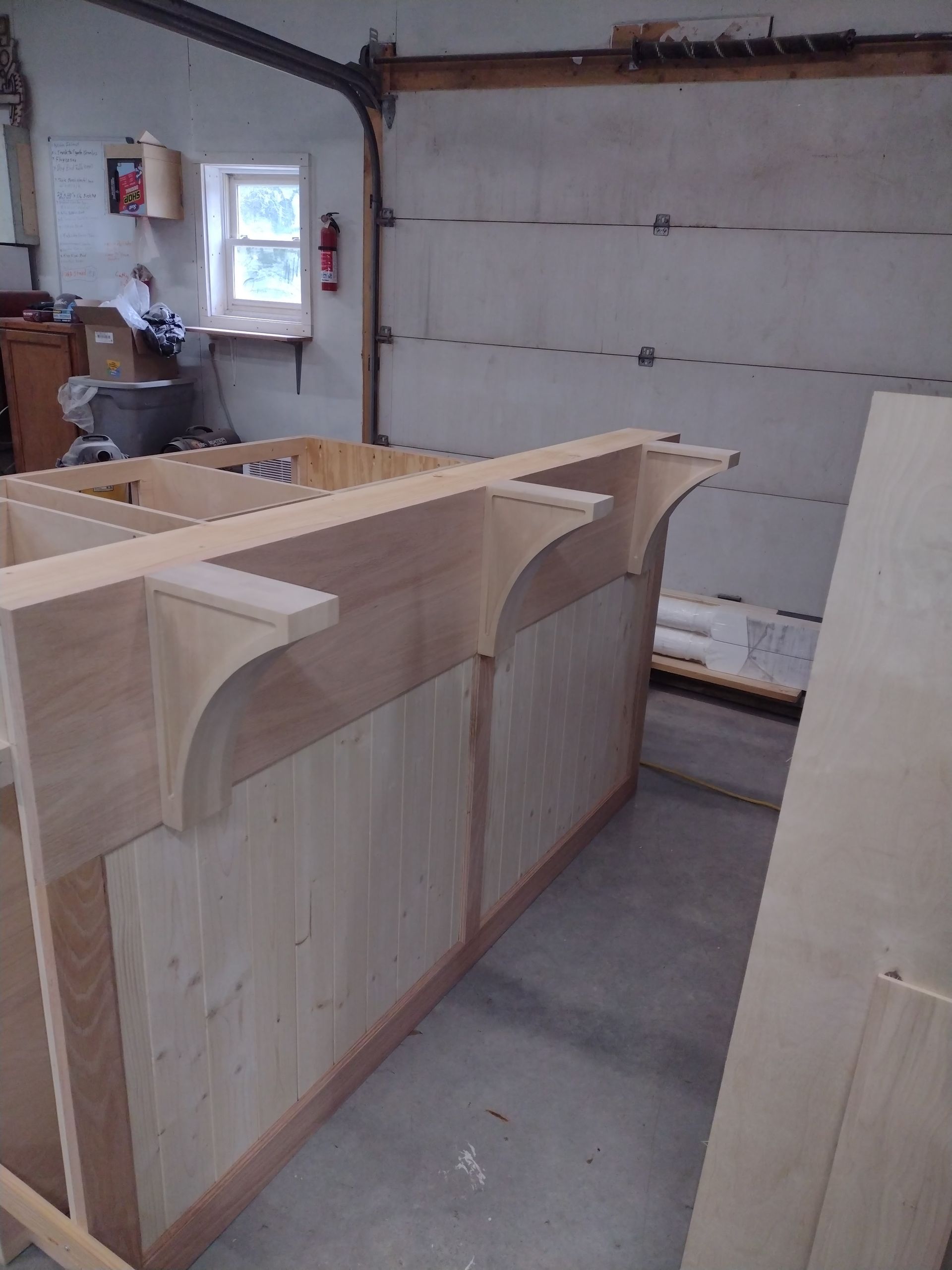 A wooden bar under construction in a workshop, featuring curved support brackets and light-colored paneling.