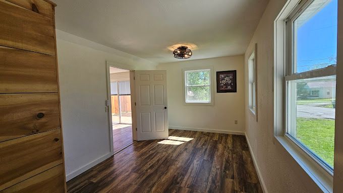 Interior of a room with hardwood floors, open door, and windows letting in sunlight.