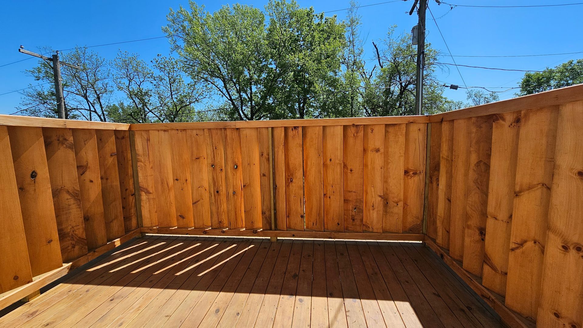 Wooden deck with a surrounding wood fence under a bright blue sky.