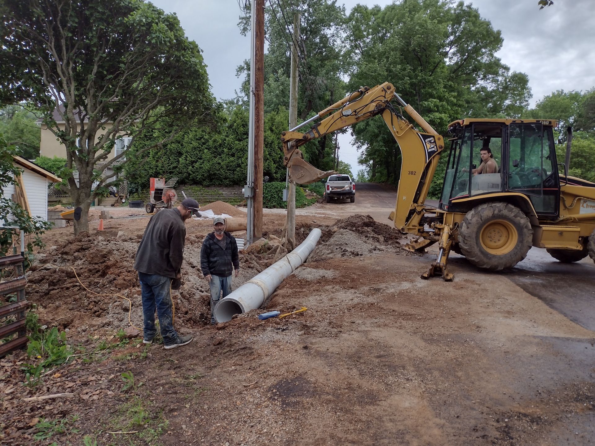 Construction workers removing a utility pole with a backhoe on a residential street.