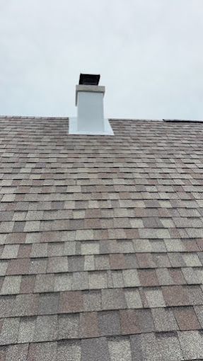 White chimney on a shingled roof against a cloudy sky.