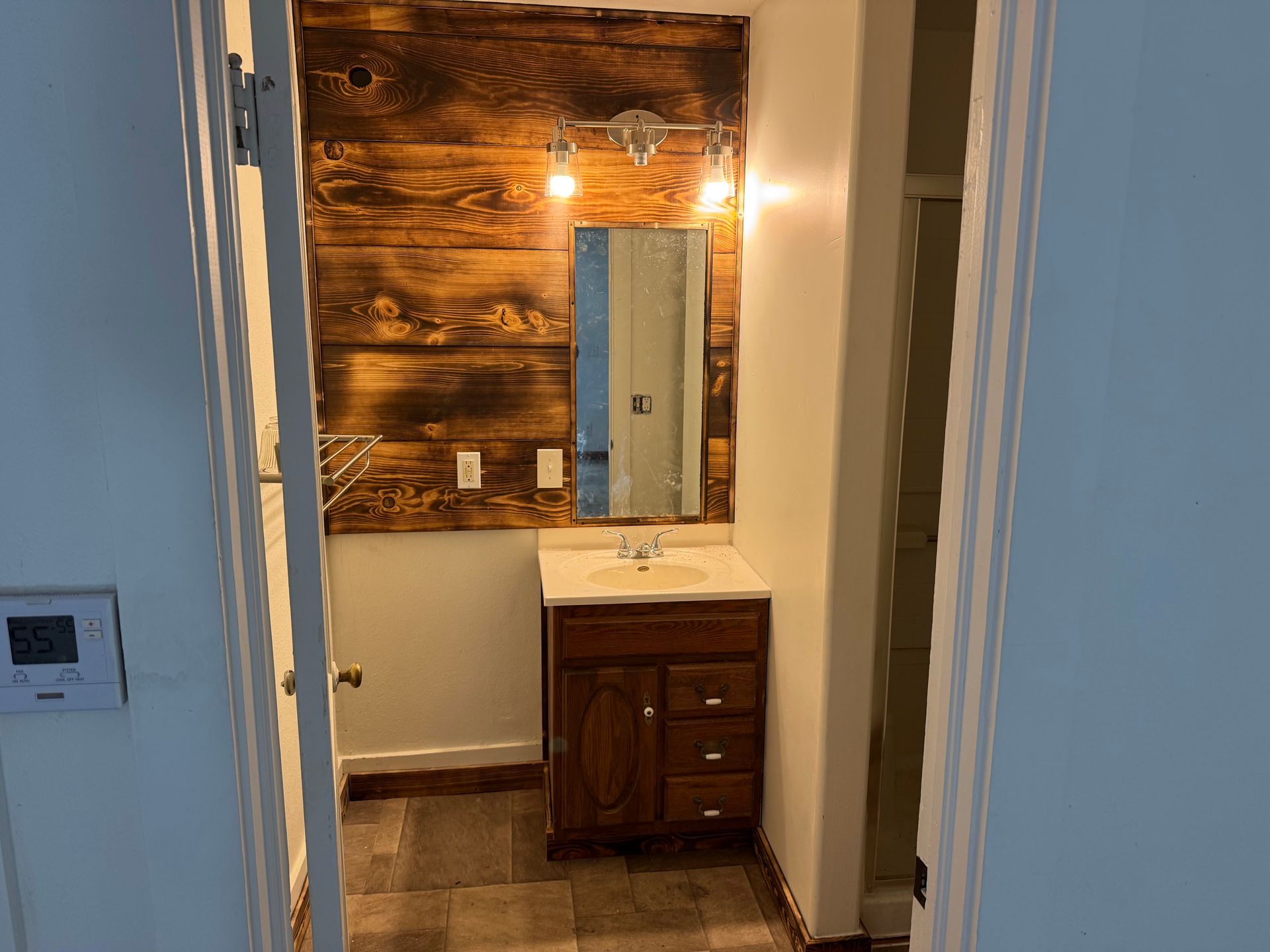 Bathroom with wood accent wall, vanity, mirror, and sconce lighting. Brown and white.