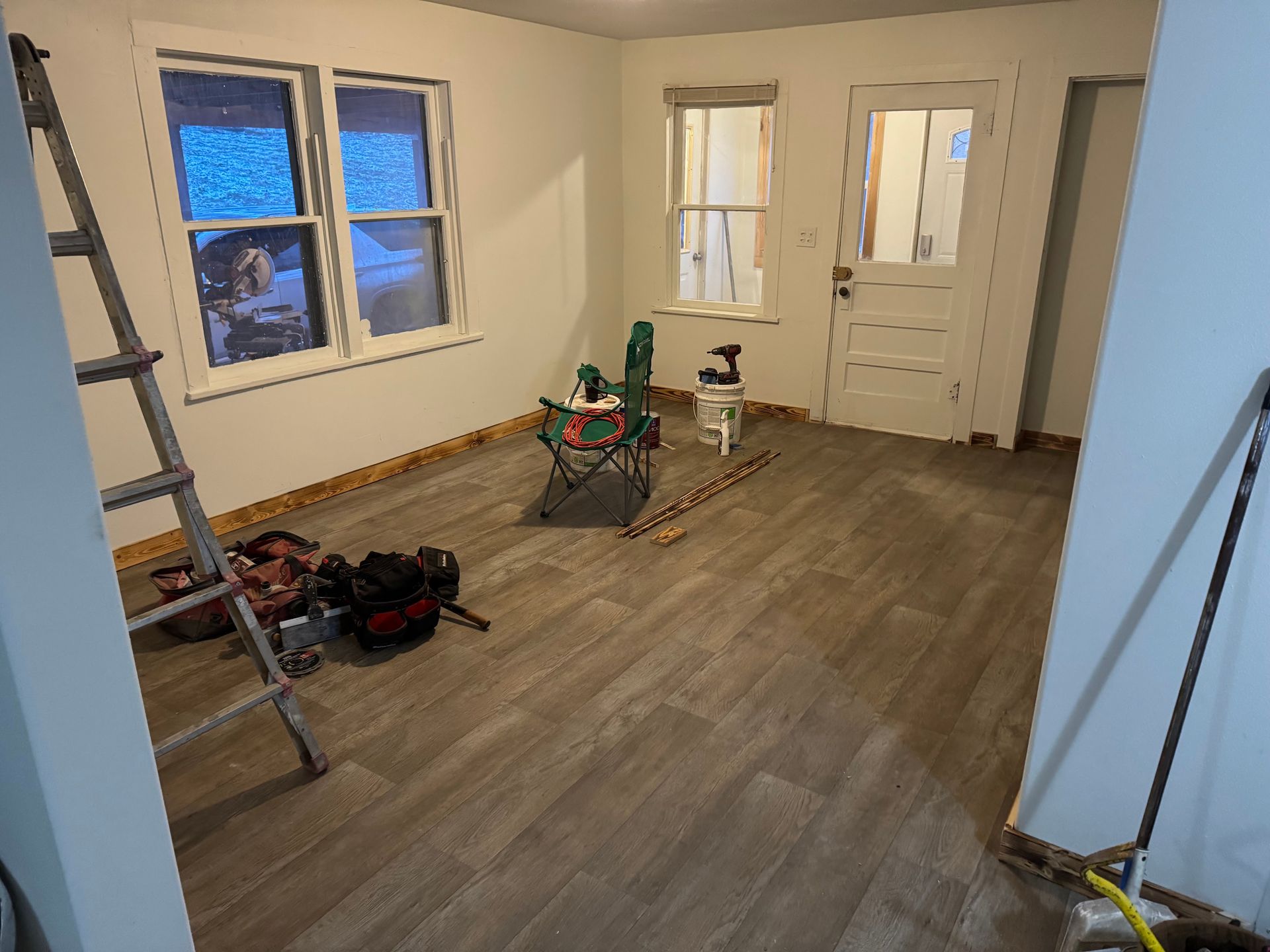 Room renovation with new flooring, tools, and partially finished walls; ladder, window, door.