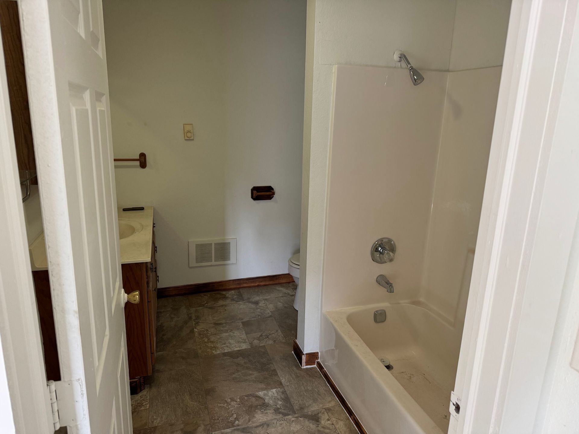 Bathroom with white tub, beige walls, and open door.