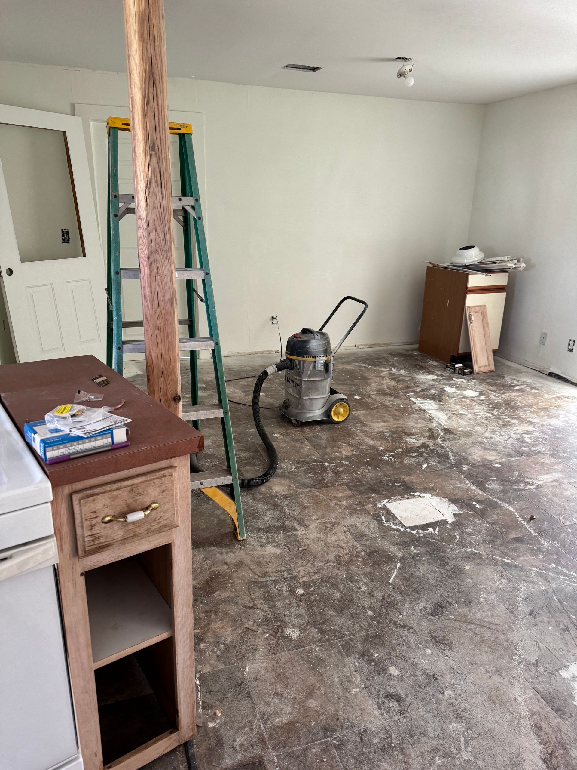 Interior renovation with ladder, vacuum, cabinets, exposed flooring and a wooden post.