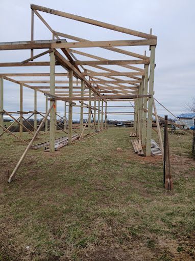 Wooden structure under construction in a grassy field on an overcast day.