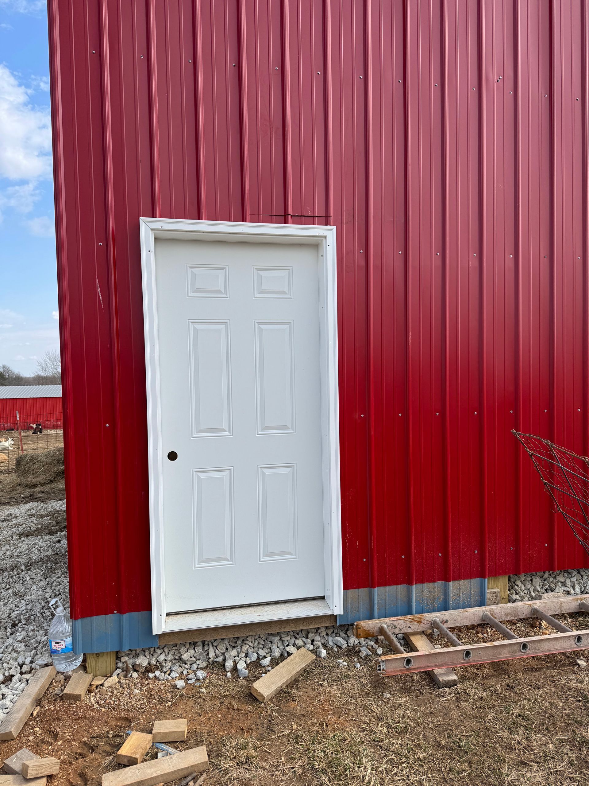 White door on a red metal building. Bricks and construction materials on the ground.