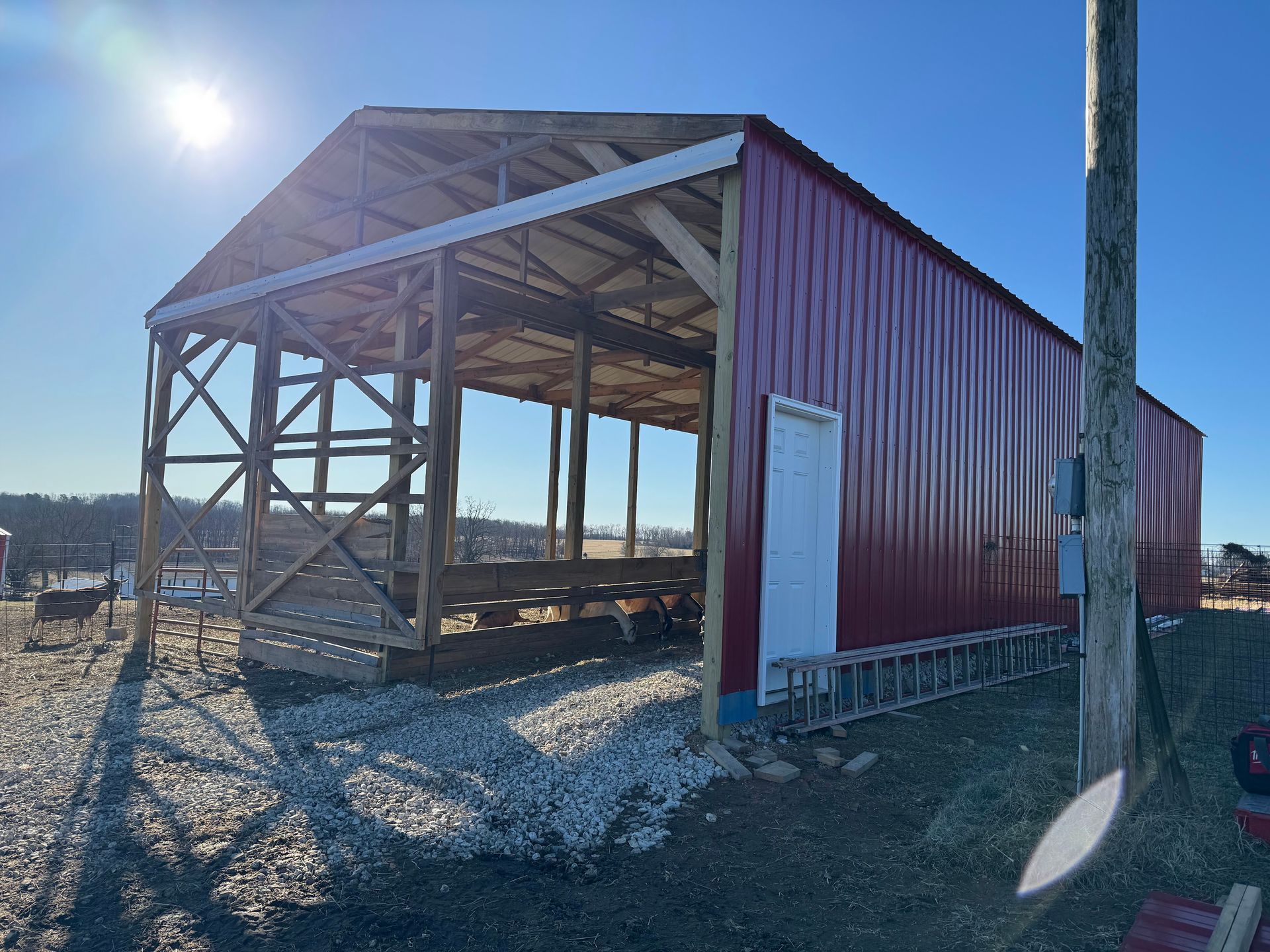 Red and white metal barn under construction with wooden frame, on a gravel lot, on a sunny day.