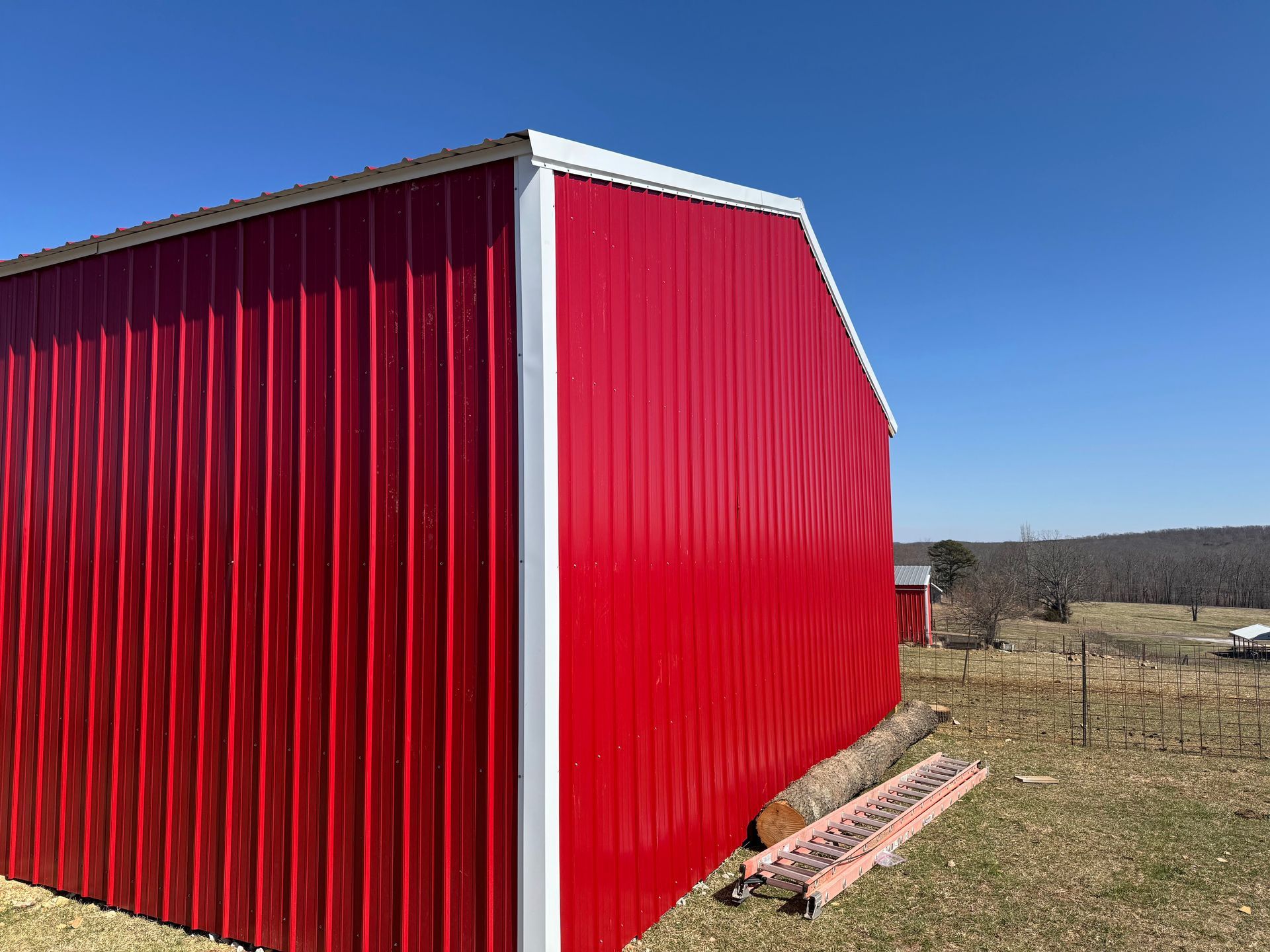 Red barn with white trim against a blue sky, set in a rural field.