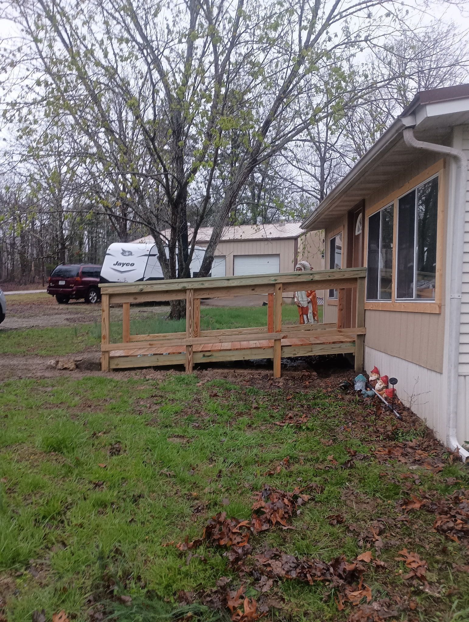 Ramp leading to a light brown mobile home. A red truck and white camper sit in the background.