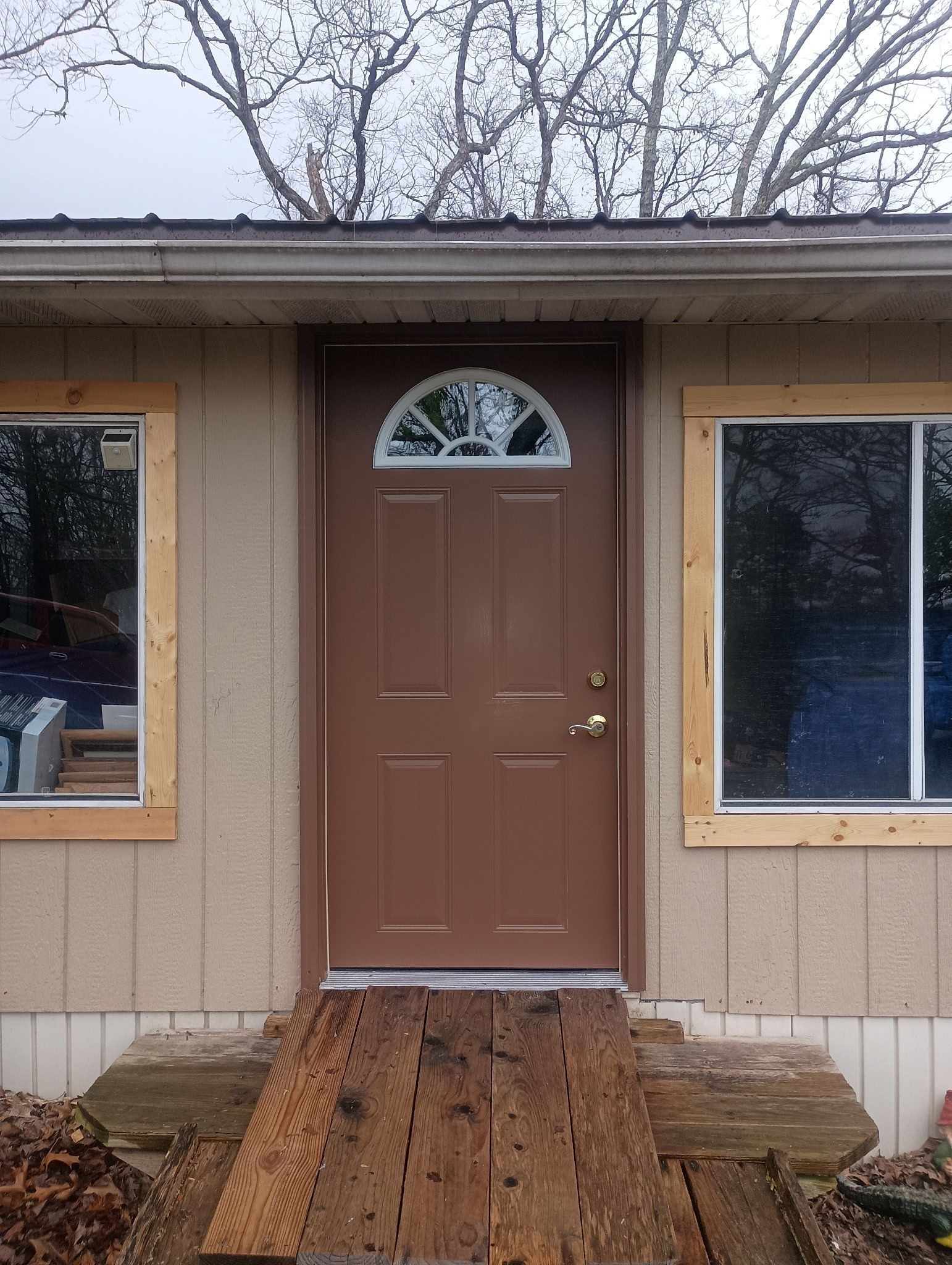 Brown door with arched window, flanked by windows, wooden ramp leading up to the door.