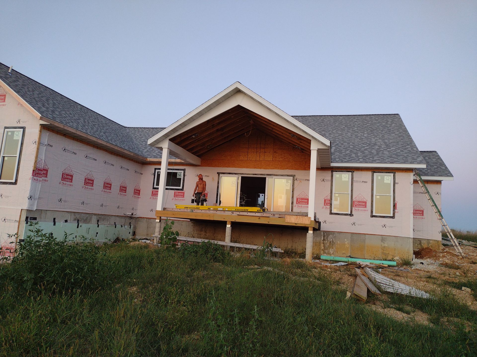 House under construction; covered porch, siding, windows, worker on deck.