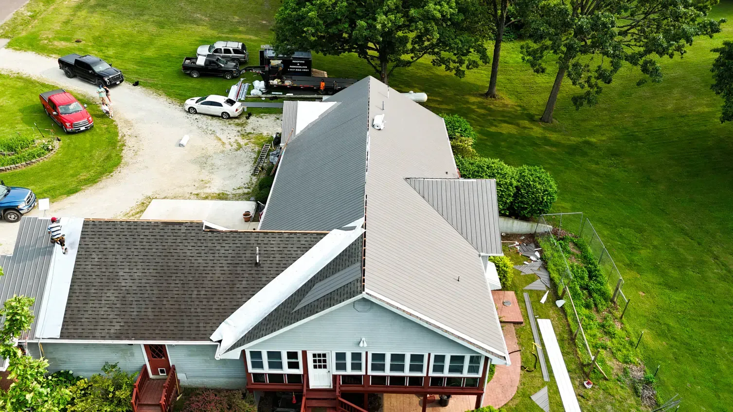 Aerial view of a house with a newly shingled roof, green grass, and parked vehicles in the driveway.