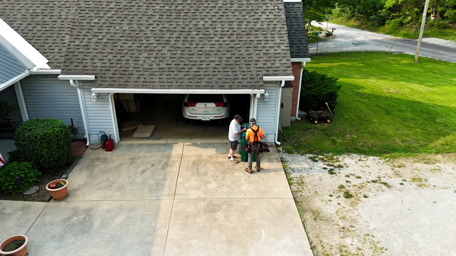 People in front of a garage; a car is inside. A concrete driveway and grassy yard are in view.