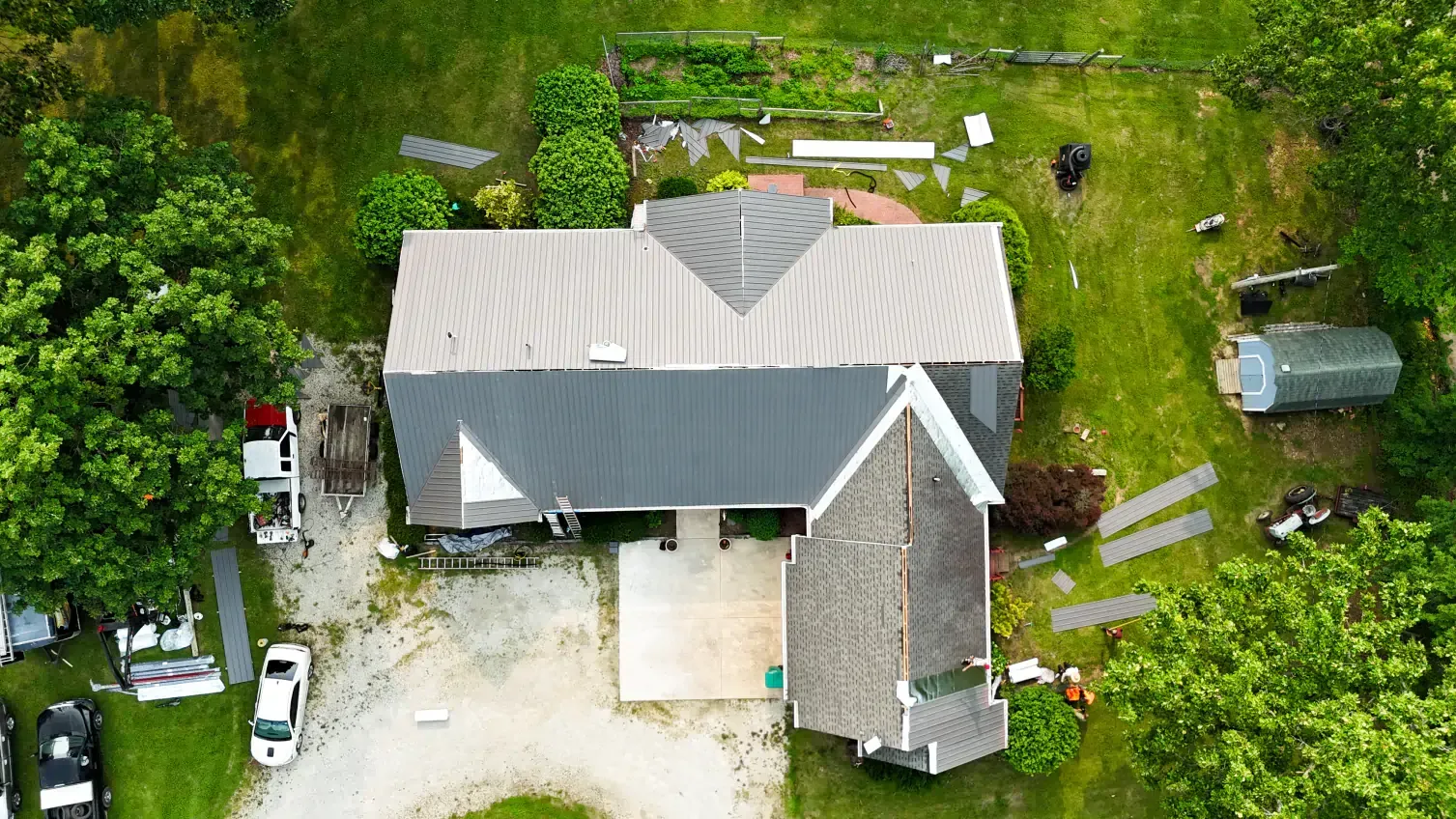 Aerial view of a gray-roofed house with a concrete patio, surrounded by green trees and lawn.