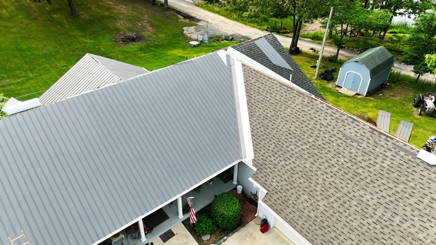 Overhead view of house with gray and tan rooftops, porch, and a blue shed.