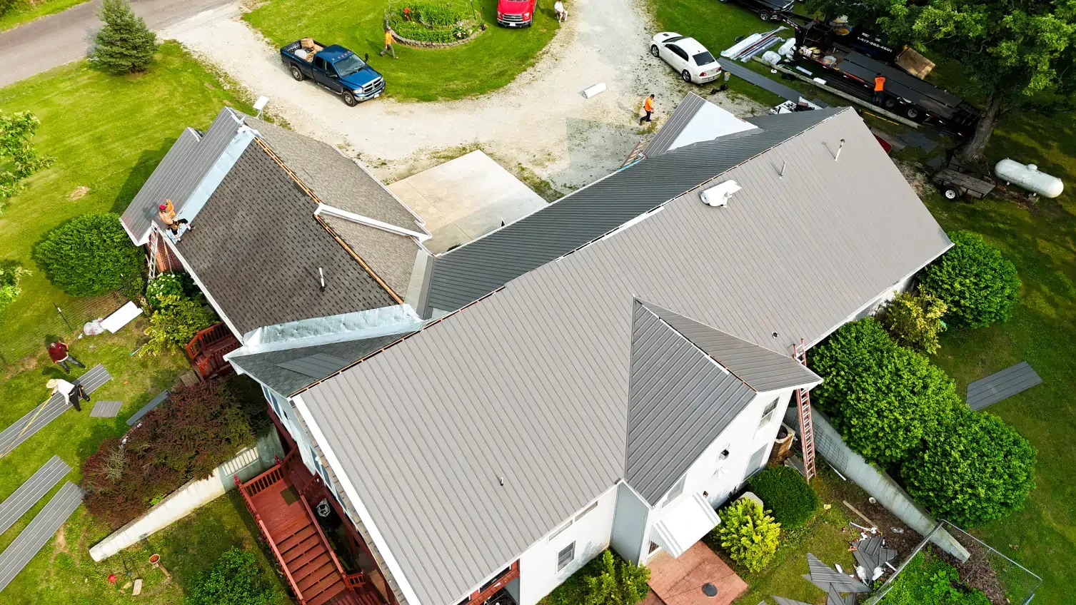 Aerial view of a house with a gray roof, surrounded by green grass and a driveway with cars.
