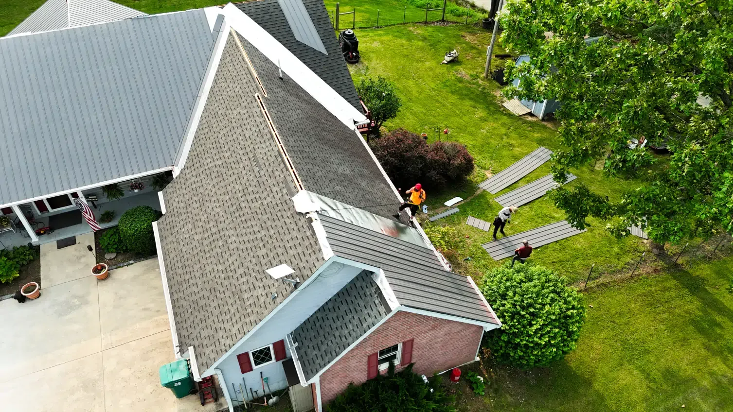 Aerial view of a house with a dark roof, yard, and people walking.