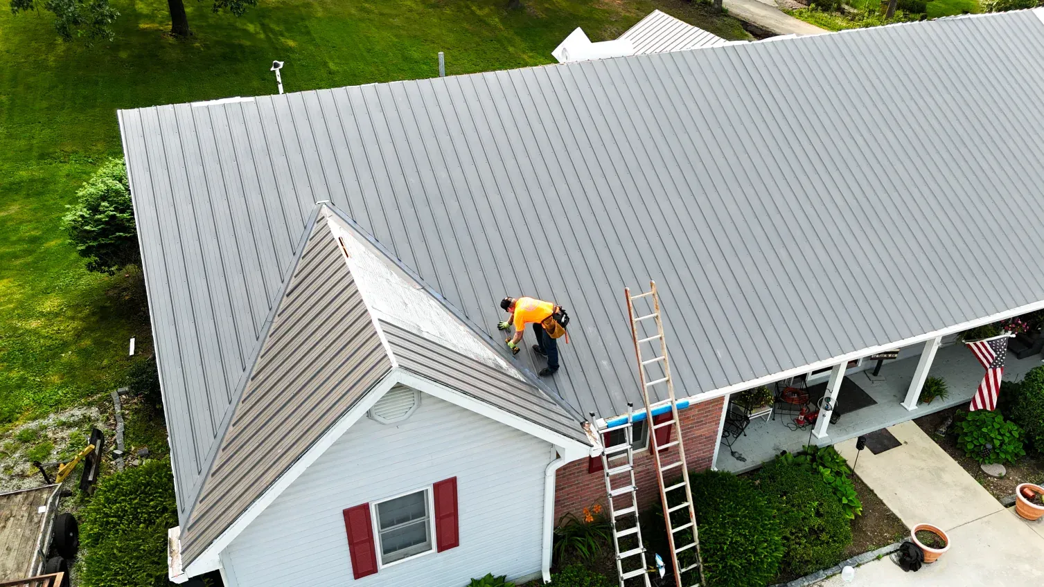 Person on a metal roof installing a new roof on a house; ladder beside the roof.