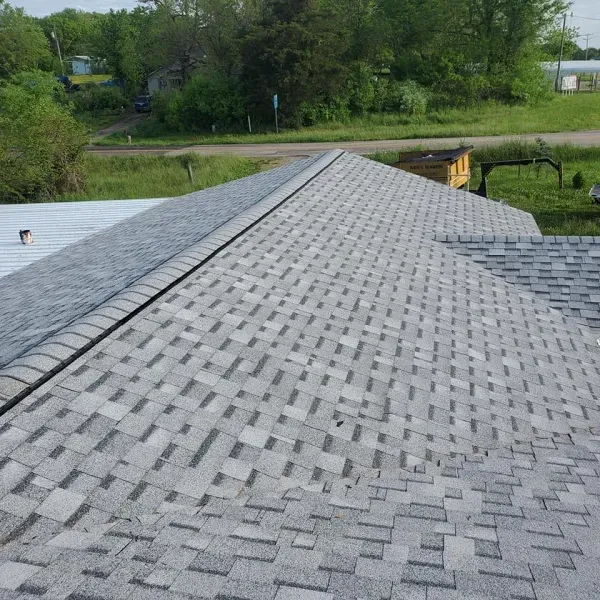 A gray asphalt shingle roof with a metal roof visible on the left; in a grassy rural setting.