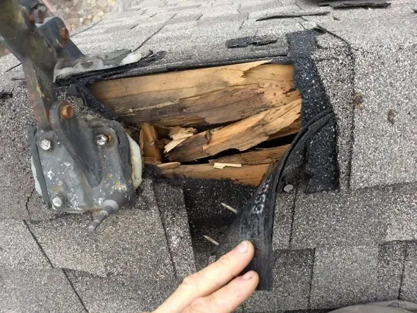 Damaged roof area with exposed rotting wood, black sealant, and a metal attachment.