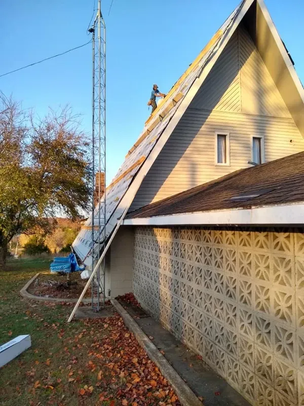 Tall radio tower next to a house with solar panels on the roof, autumn leaves on the ground.